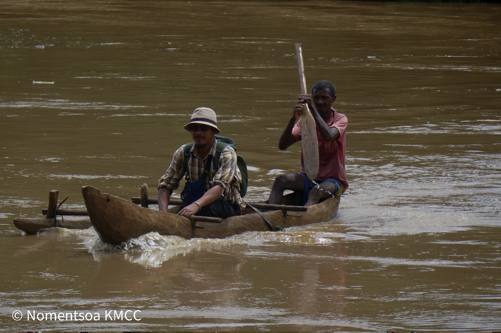 Two men in a dug-out canoe crossing a wide river